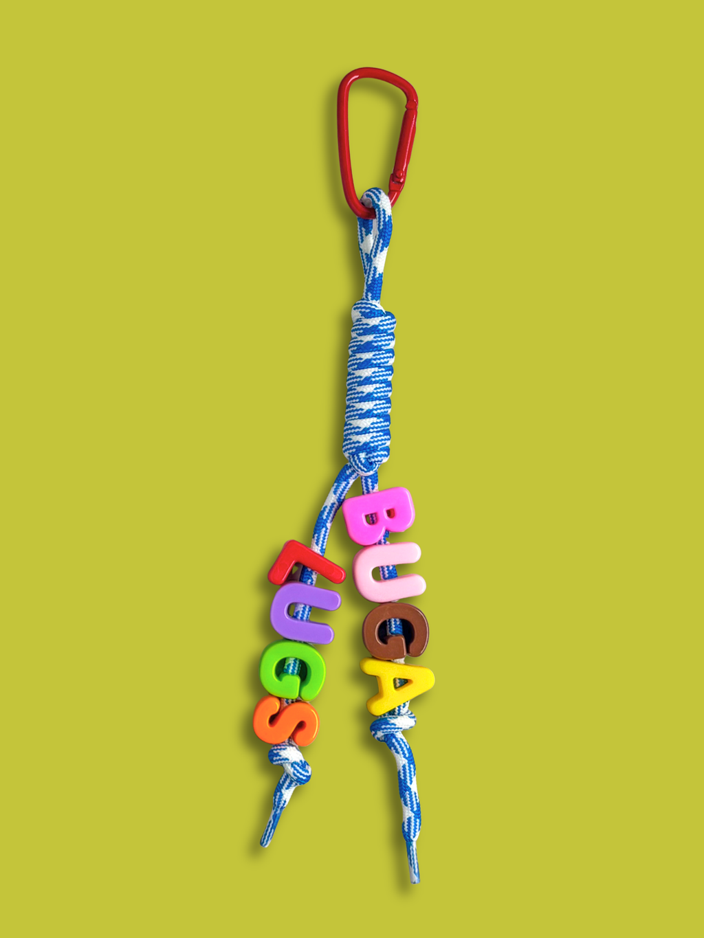 Custom statement bag charm with letter beads spelling BUGALUGS in pink, brown, yellow, red, purple, green and orange, threaded across two strands of a blue and white houndstooth knotted cord with a red carabiner clip, on a green background. Made by Bugalugs in Melbourne.