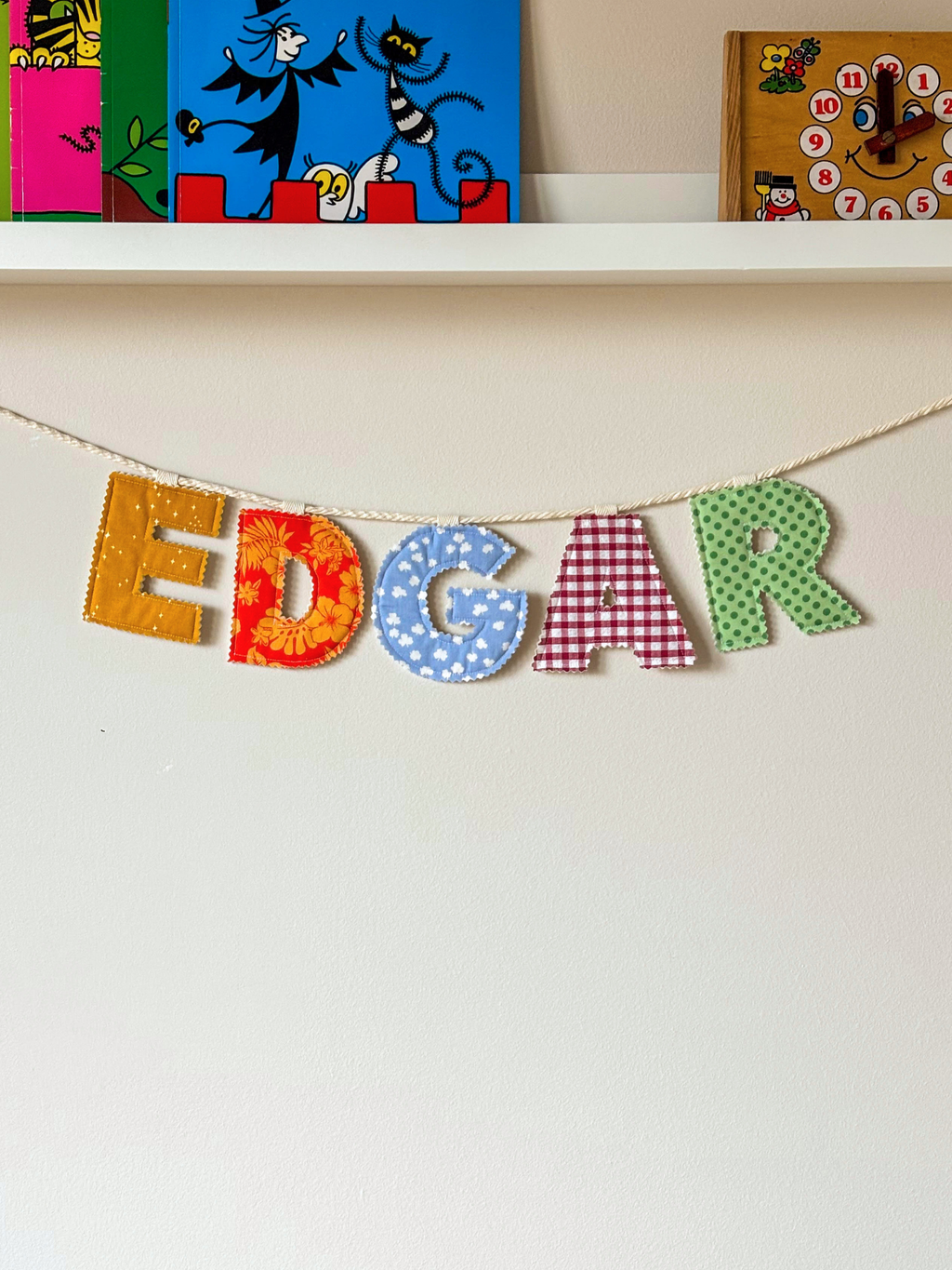 Personalised name banner spelling 'EDGAR' in bright fabrics on a white wall. Made by Bugalugs in Melbourne. 