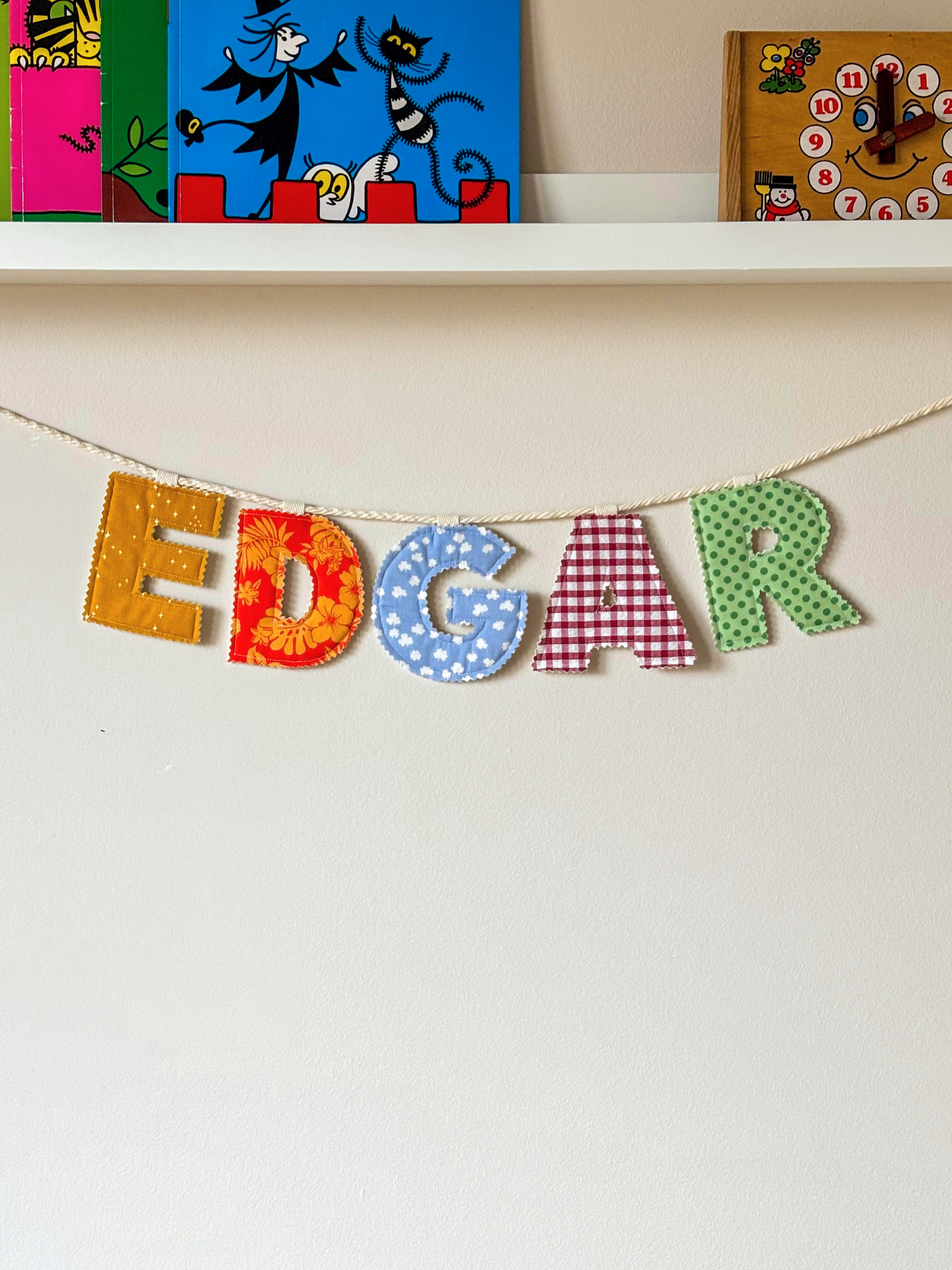 Personalised name banner spelling 'EDGAR' in bright fabrics on a white wall. Made by Bugalugs in Melbourne. 
